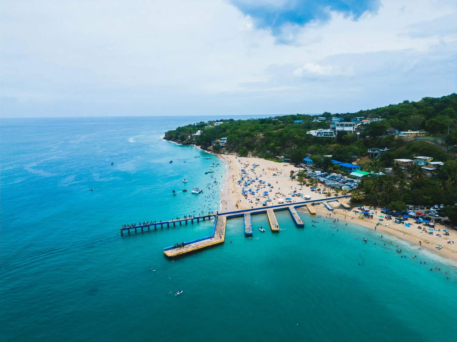 A turquoise bay with a pier and swimmers seen from above.